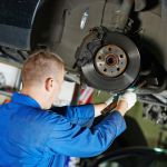 33211449 - car mechanic worker repairing suspension of lifted automobile at auto repair garage shop station